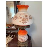 Antique electric hurricane-style table lamp with frosted glass body and shade, orange gradient trim, brown floral decoration, clear glass chimney and ornate brass-tone metal base.