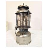 Coleman Quick-Lite pressure lantern marked 7/26, with silver-tone fount and ventilator, clear globe and wire bail handle. Shows age-related oxidation and wear.