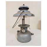 J.C. Higgins Model 710.74010 pressure lantern with blue-gray painted fount and matching ventilator, clear globe and wire bail handle. Shows paint loss, oxidation and age-related wear.