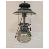 Coleman Model 228D “Big Hat” pressure lantern marked A/49, with silver-tone fount, wide green porcelain ventilator, clear glass globe and wire bail handle. Shows oxidation and age-related wear.