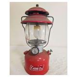 Coleman Model 200A pressure lantern with red fount and red porcelain ventilator, clear Coleman Pyrex globe and wire bail handle; marked 2/79. Shows decal damage, surface wear and age-related use.