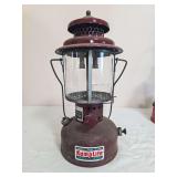 Kamplite Model RL-3 pressure lantern with dark maroon fount and matching porcelain ventilator, clear globe and wire bail frame. Shows finish wear, dust and age-related use.