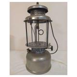 Coleman Quick-Lite pressure lantern with silver-tone fount and ventilator, clear Pyrex globe and wire bail handle. Shows age-related oxidation and finish wear.