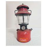 Vintage Coleman Model 200A pressure lantern with red painted fount, matching red ventilator, clear glass globe and black wire frame; marked 6/52. Coleman decal remains visible on the fount with paint 
