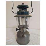 Coleman Model 242C Lantern – Marked 5/48. Vintage single-mantle pressure lantern with nickel-tone fount, green porcelain ventilator, clear globe and wire bail handle; shows oxidation and age-related