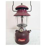 Coleman Model 200A pressure lantern with dark maroon fount and red/maroon porcelain ventilator, clear Coleman globe and wire bail handle; marked 1/62. Shows decal wear, surface wear and age-related us