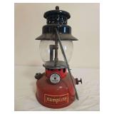 Kamplite Model LRL-21A pressure lantern with red fount, black porcelain ventilator, clear globe and wire bail handle. Shows paint wear, oxidation and age-related use.