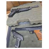 Three pellet pistols in foam-lined hard case, including a Gamo P-23 and two long-barrel target-style pistols identified in the catalog as Daisy and Silhouette. Includes black and wood-tone grip/forear
