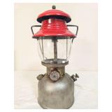 Coleman Model 200 pressure lantern marked 1/51, with silver-tone fount, red porcelain ventilator, clear globe and wire bail handle. Shows age-related surface wear and oxidation.