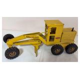 Vintage Tonka pressed-steel Road Grader in yellow with six rubber tires and adjustable center grading blade. Shows paint wear and age-related use.