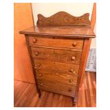 Oak five-drawer dresser/chest with shaped backsplash, wood knobs, keyholes and tall narrow form. Shows age-related surface wear and finish marks.