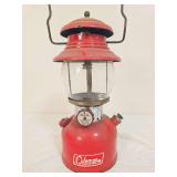 Coleman Model 200A pressure lantern marked 8/71, with red painted fount, matching red porcelain ventilator, clear Coleman globe and wire bail handle. Shows paint wear, soiling and age-related use.