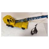 Vintage Michigan Model T-24 toy crane with yellow body, blue lattice boom and suspended clamshell bucket. Shows age-related paint wear and surface oxidation.