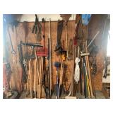Assorted Garage and Yard Tools Including Rakes, Saws, Shovels, and Post Hole Digger