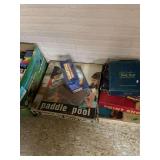 Assorted Lot of Board Games and Media Box including Paddle Pool, Trivial Pursuit, and VHS Tapes