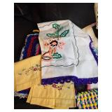 Collection of handcrafted textiles including embroidered linens, crocheted potholders, Rug and More