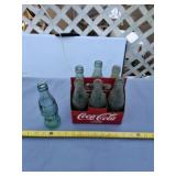 7 empty Coca Cola bottles and holder