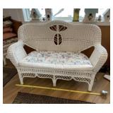 Wicker loveseat with cushions and pillows.