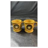 Two yellow ceramic mugs featuring raised USCGC