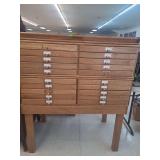 lot contains a  vintage oak multi-drawer file cabinet, often referred to as a map, blueprint, or printer's cabinet. These cabinets were historically designed to store large documents or specialized it