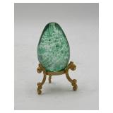 Green speckled glass egg paperweight on stand,