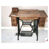 SINGER TREADLE SEWING MACHINE - WOOD CABINET - 4 DRAWERS WITH BRASS LION HEAD PULLS - END TRIM LOOSE - GOOD FINISH SOME VENEERING WORN AND RIPPLED - ATTACHMENT BOX - (MASTER BEDROOM)