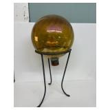 Marigold colored glass gazing ball sits in a
