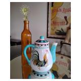 Bob Mackie Home Rooster Earthenware Teapot. Amber glass bottle featuring a square-shaped body, a round neck, and a unique decorative stopper.