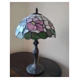 Tiffany style table lamp features a stained glass shade with a floral motif and a decorative metal base. 20" T x 12" across shade.