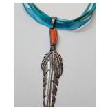 Native American-inspired feather pendant necklace, featuring a detailed Sterling feather pendant and a small red coral  accent.  It is strung on a multi-strand blue ribbon and cord. 925 silver clasp. 