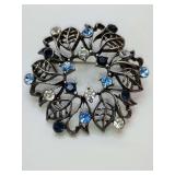 Silvertone wreath brooch with leaves, clear, light blue & dark blue rhinestones 2" wide.