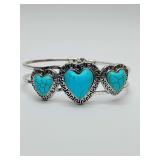 Southwest-style clamp bangle bracelet heart-shaped stones in a turquoise color, set within a silver-tone frame. Central heart flanked by two smaller hearts, each surrounded by an intricate Greek key p