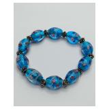 Blue glass bead stretchy bracelet, with Murano style lampwork with pink floral and white swirl designs, and silvertone metal spacers.