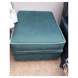 Green canvas ottoman on casters with white piping around top and bottom of cushion. 32 x 25 x 18 in tall.