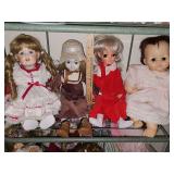 Shelf of dolls. Two dolls on left are porcelain. One on far left has a stand. Two dolls on right are rubber dolls.