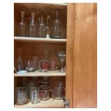 Group of glass ramekins, measuring cups, and corked bottles with a few glass stems.