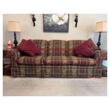 Traditional scroll arm three-seater sofa upholstered in a red, green, and gold plaid fabric with a pleated skirt base and matching burgundy accent pillows