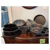 Contents on top shelf of cabinet by refrigerator of nice bakeware.