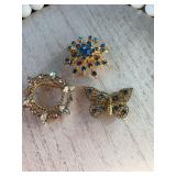 Two blue rhinestone and gold tone brooches and one clear and gold tone brooch