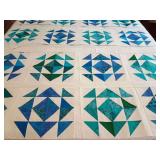 Machine stitched quilt top in 4 pieces. Half-square triangles (HSTs) arranged in a pinwheel and star block design with an ocean-themed palette of teal, turquoise, and blue batiks paired with white sas