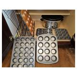 Cabinet contents. Includes cupcake or muffin pans, mini muffin or cupcake pans, cooling rack, and Hamilton Beach crock-pot.