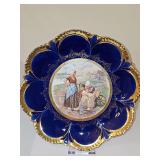 Empire China porcelain cabinet plate featuring a deep cobalt blue and heavy gilt-scalloped rim, centered with a transfer-printed pastoral scene of figures in traditional attire. Crazing on back of pla