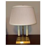 Brass bouillotte-style candlestick table lamp featuring a polished brass finish, two artificial candle sleeves, a central column, a square base, and a pleated fabric lampshade - 17” tall
