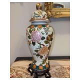 Decorative hand-painted porcelain or ceramic lidded ginger jar/temple jar with a cream or crackle-glaze background and colorful floral, foliage and butterfly motifs sitting on wood stand - 15 tall inc