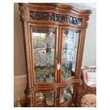 EXQUISITE Lighted Michael Amini AICO Paradisio China Curio Cabinet, crafted from hand-carved wood. Features an ornate, sweeping scrollwork and floral carving at the top crown with glass-front display 