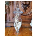 Glass footed apothecary jar with a matching lid, filled with sea shells and drift wood. 18 in tall.