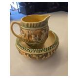 Roseville Donatello art pottery pitcher and bowl set, introduced around 1916. Design: Features a sculpted cherub (putti) relief decoration in a landscape setting with soft, blended colors on a cream o