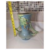 Roseville Blue Bushberry handled vase, likely model 34-8, introduced around 1941. 
Design: Features a molded berry and leaf pattern on a blue stippled background with characteristic angular handles