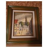 Framed oil painting depicting a European cityscape scene with buildings and a central church tower-15x17