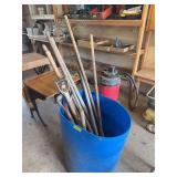 Long handled yard tools and a blue barrel